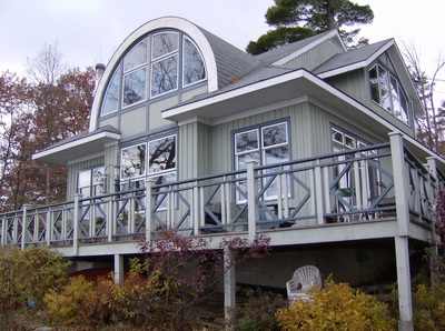 River front view of a custom home with a large semi-circle dormer, all glass in front.